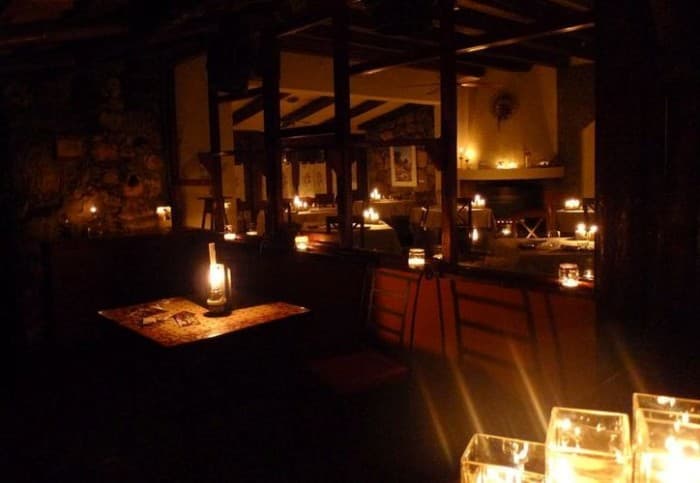 Interior de restaurante iluminado solo con velas durante un apagón, mostrando mesas y barra con luz artificial mínima.