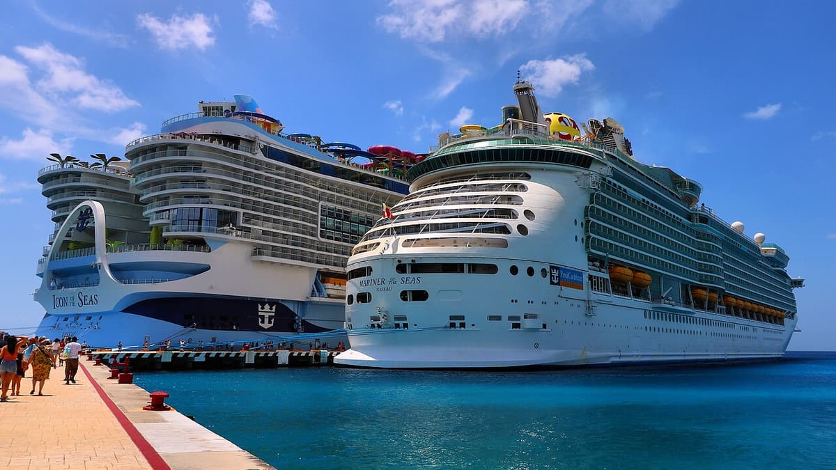 Dos cruceros de Royal Caribbean atracados en un puerto tropical con aguas turquesas y pasajeros en el muelle.
