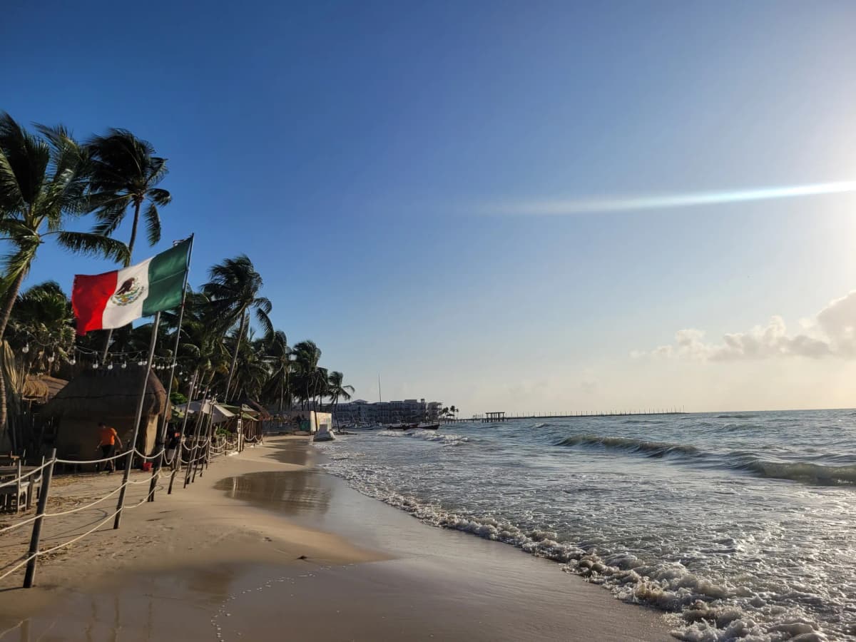 Playa de Playa del Carmen con palmeras y una bandera de México junto al mar
